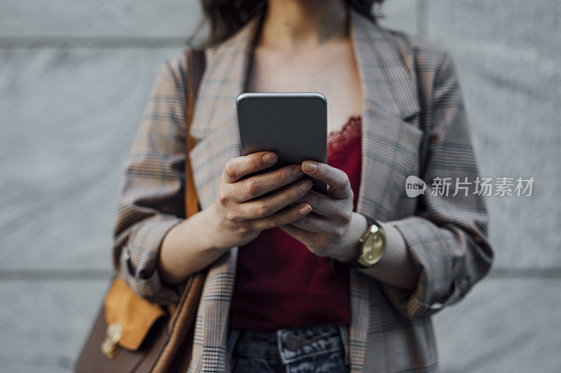 Business on the Go: Hands of an unrecognized Businesswoman Using a Mobile on the Street, a Close Up .(商业上:一个不认识的女商人在大街上使用手机的手，一个近距离观察。